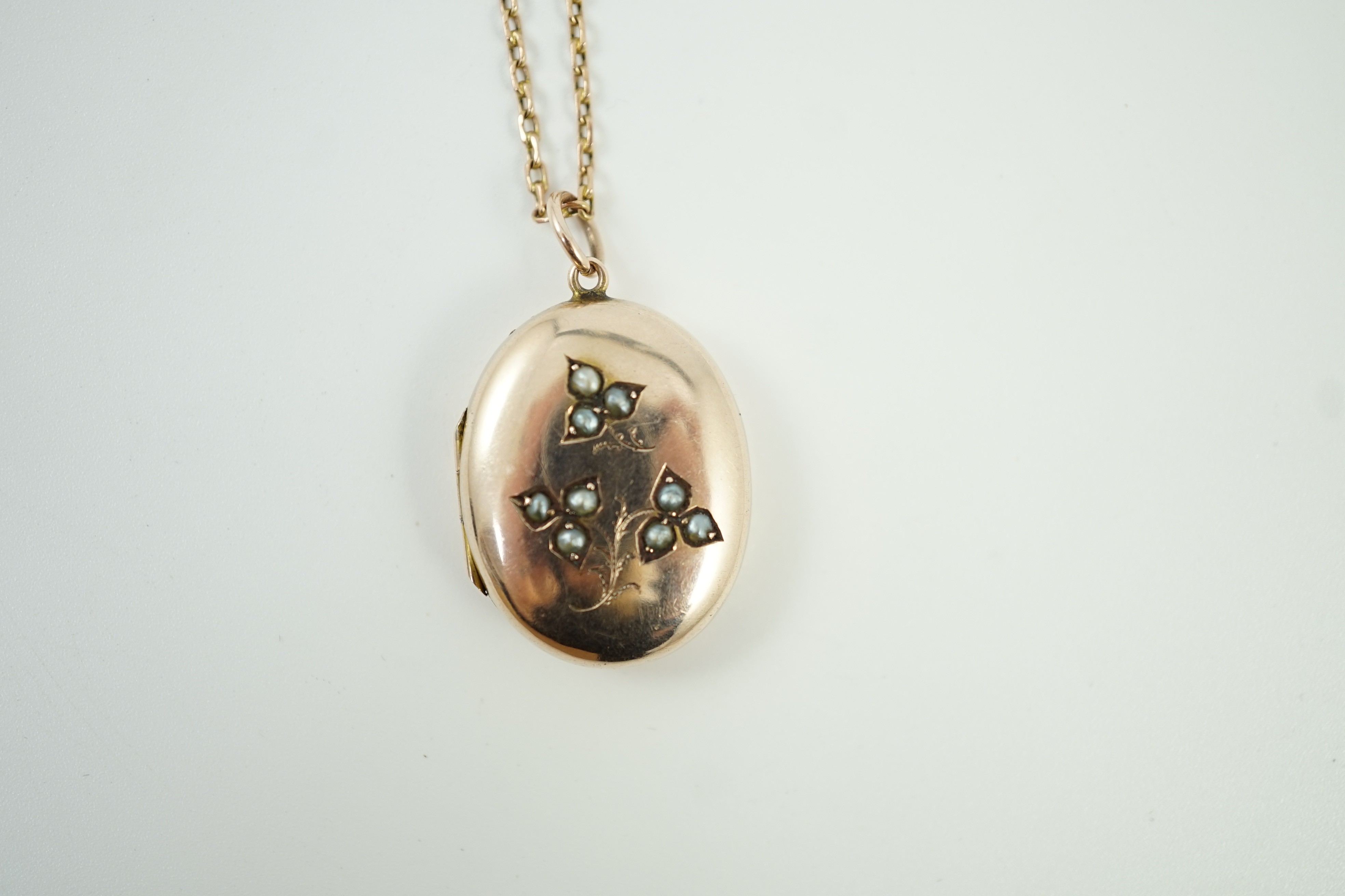 An Edwardian yellow metal and seed pearl set oval locket pendant, 25mm, on a 9ct chain, 47cm, gross weight 9.3 grams.